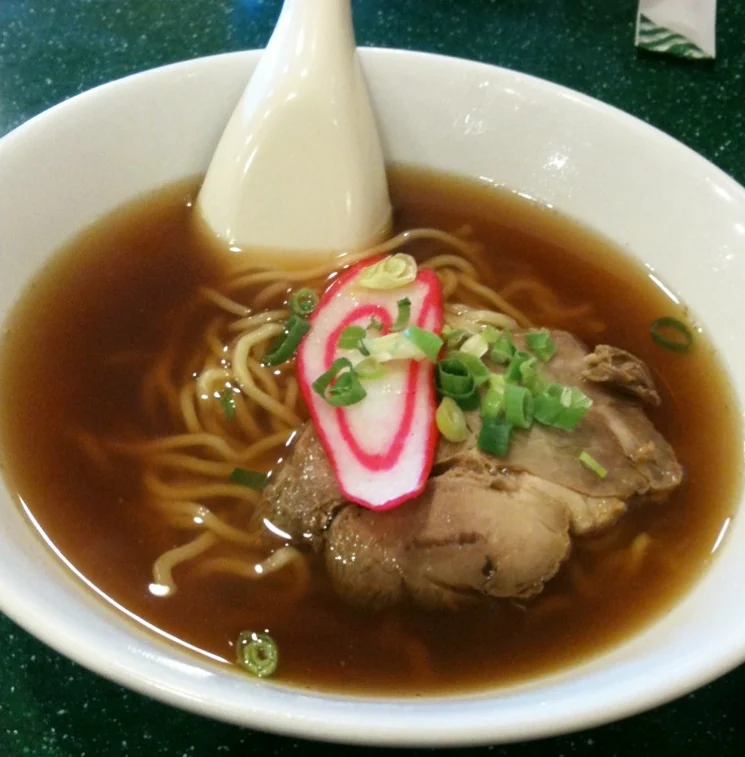 A small ramen bowl with noodles, fish cake, scallions and sliced meat.