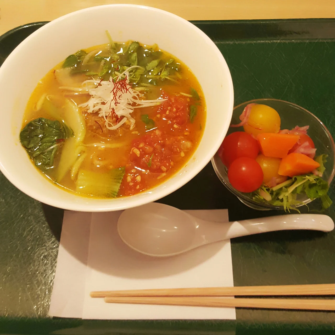 A vegetable-topped bowl with greens, carrots and red seasoning, with a side of vegetables.