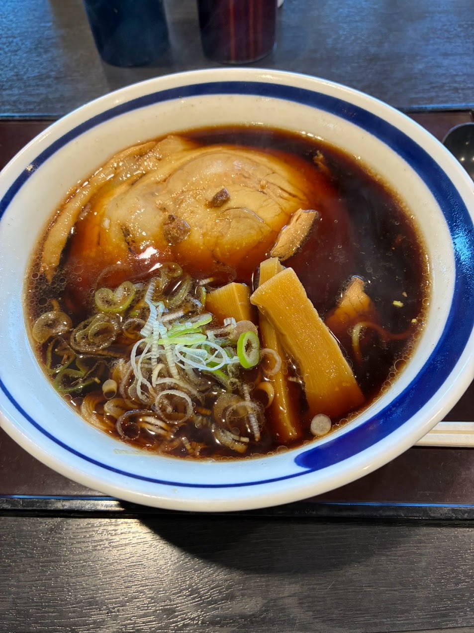Toyama Black ramen at Arisoumi Service Area, with dark brown broth, a large slice of chashu pork, bamboo shoots and sliced green onions in a blue-rimmed bowl.