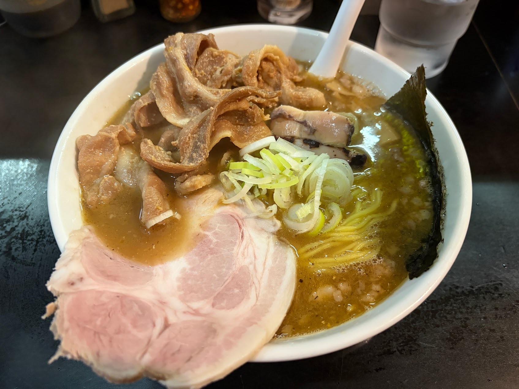 Ganko ramen in a wide white bowl: golden cloudy broth, a generous pile of folded pork, large chashu slices, scallions, nori and thin yellow noodles.