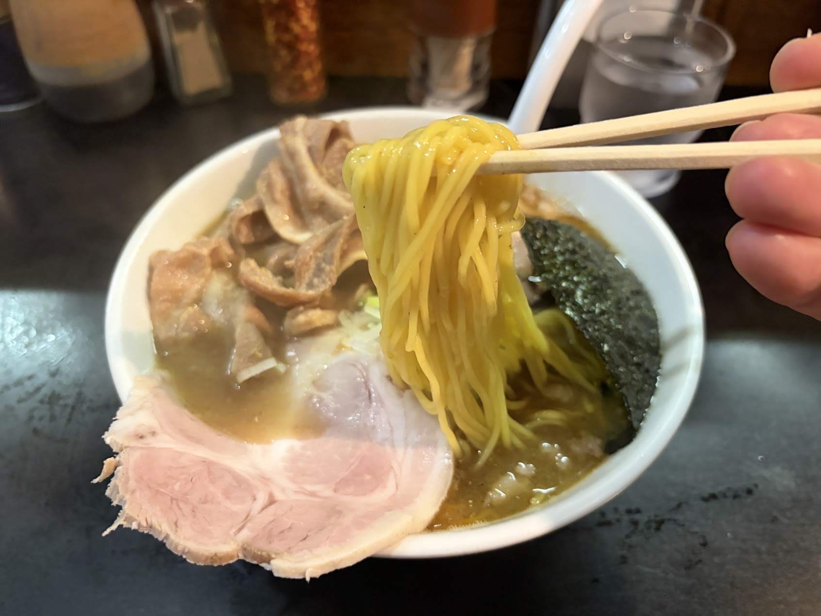 Chopsticks lift thin yellow noodles above the Ganko ramen, with folded pork, chashu and nori below.