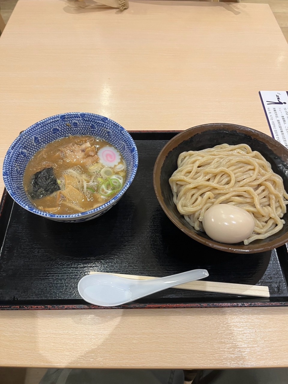 Rokurinsha tsukemen on a black tray: blue-patterned dipping-soup bowl beside a dark-brown bowl of thick noodles and a whole egg.